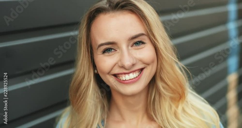 Portrait of the charming young woman with blond hair giving her amazing sincere smile tothe camera. Close up. Outdoor. photo