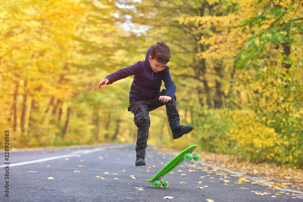 Fototapeta premium Kid skateboarder doing skateboard tricks in autumn environment