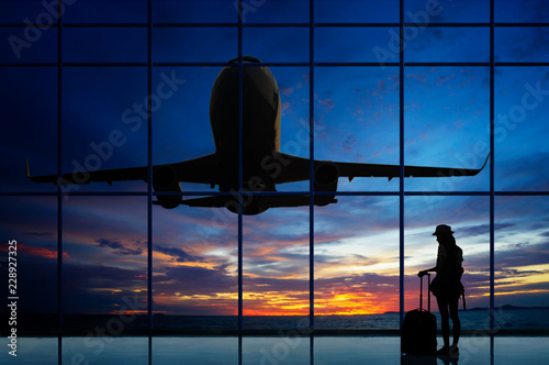 Young woman is standing near window at the airport and watching plane before departure.