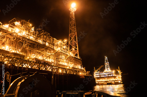 FPSO tanker vessel near Oil platform Rig. Offshore oil and gas industry, sea oil production and storage. Flare boom is brightly burning at night. photo