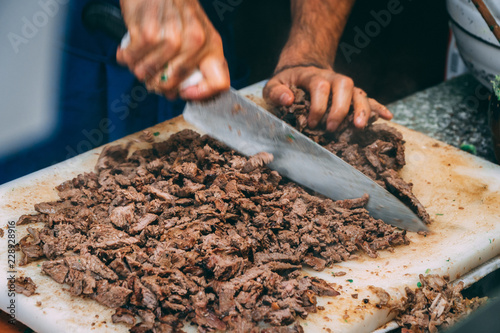 Close up of chef chopping carne asada on a plastic cutting board with a blurry in motion chefs knife photo