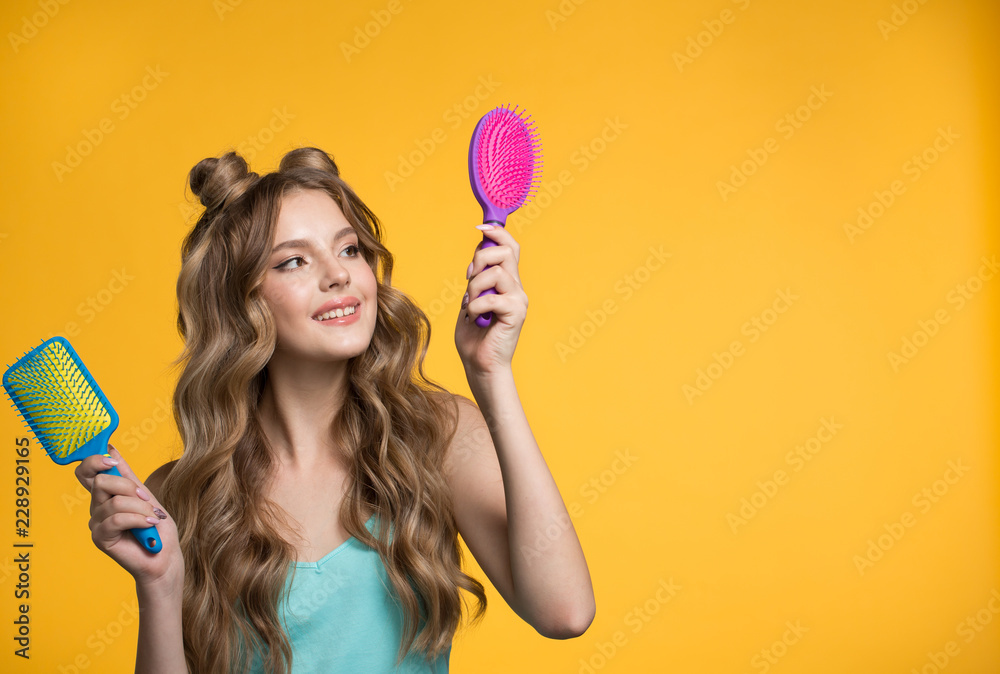woman is holding a comb. Woman on yellow background with curly long hair. woman is holding a comb. Woman on yellow background with curly long hair.