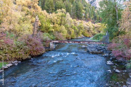 Fast flowing Jordan river in Utah lined with autumn foliage trees of orange  red and yellow with rail bridge