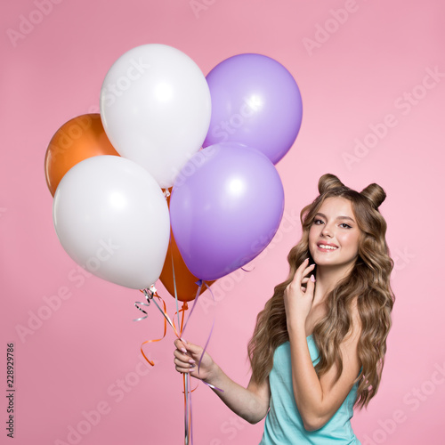Woman holding pink balloons over pink background. Beautiful woman with long wavy hair smiling