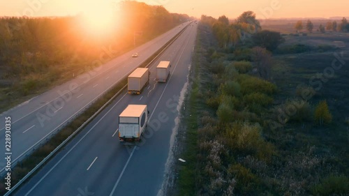 Aerial view of white semi trucks with cargo trailer are moving on the highway at sunset. Back view photo