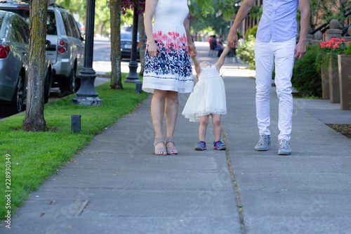 Parents, husband and wife, walk with their girl toddler kid down the alley on idyllic summer day.