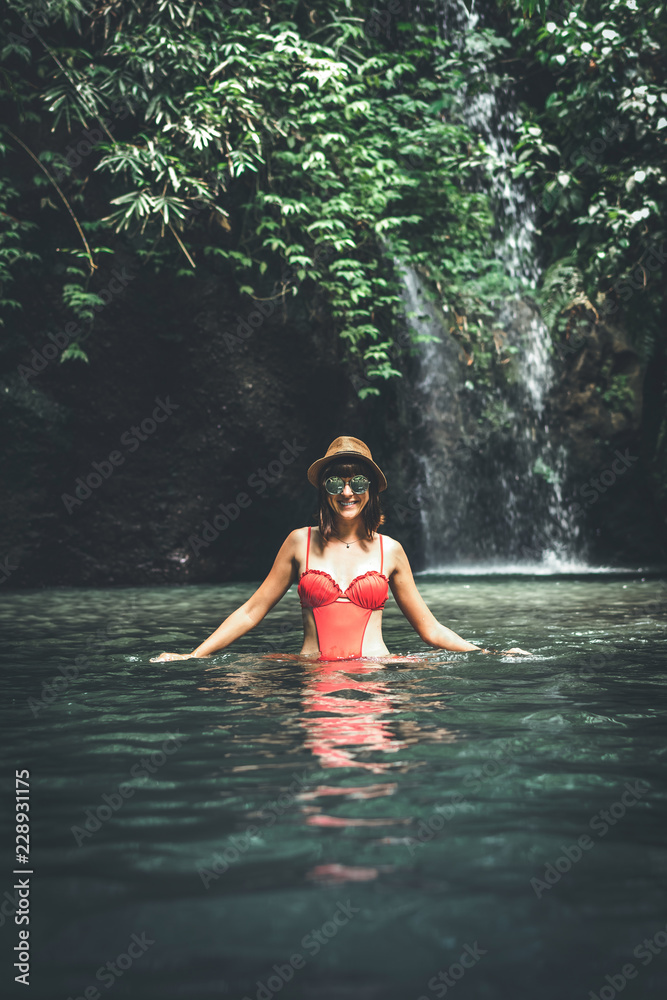 Young woman tourist with straw hat in the deep jungle with waterfall. Real adventure concept. Bali island.