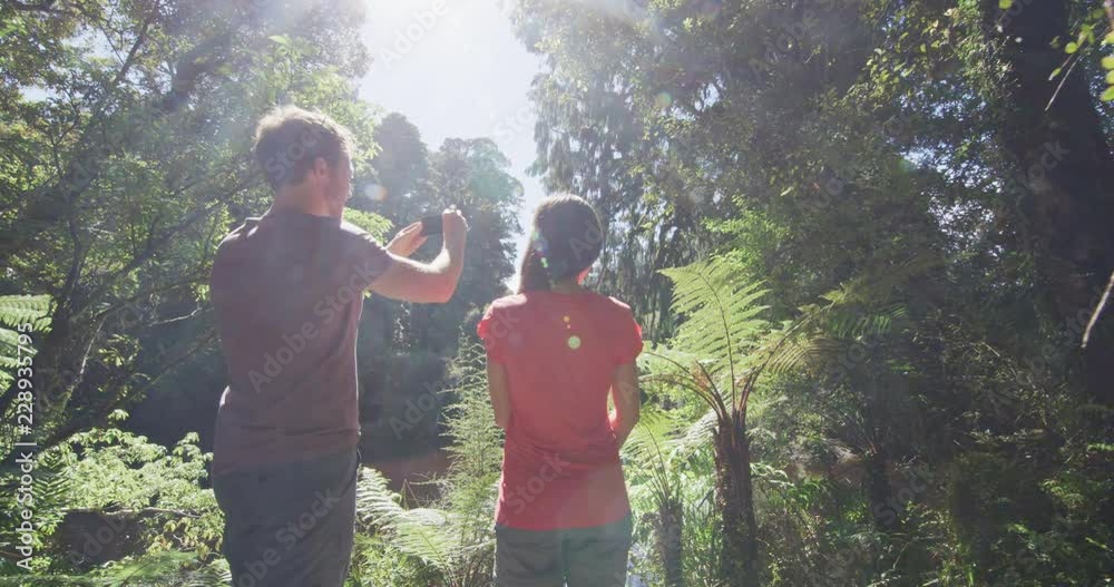 Hiking people in New Zealand swamp forest taking mobile phone pictures in Ship Creek on West Coast of New Zealand. Tourist couple sightseeing tramping on South Island of New Zealand. Hiking people in New Zealand swamp forest taking mobile phone pictures in Ship Creek on West Coast of New Zealand. Tourist couple sightseeing tramping on South Island of New Zealand.