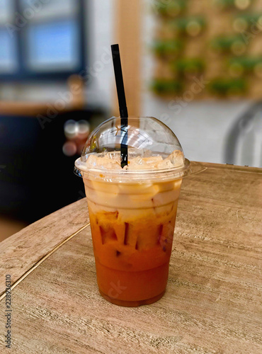 takeaway plastic cup of cold milk Thai tea with ices on wooden table at coffeeshop