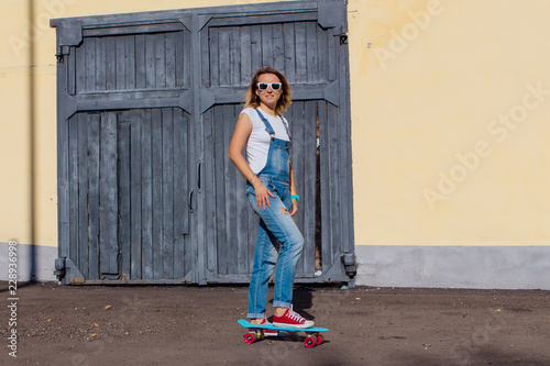 Portrait of a smiling woman standing with her skateboard next to the old wooden wall.