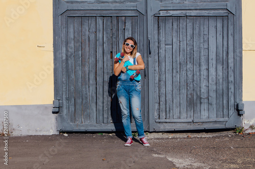 Portrait of a smiling woman standing with her skateboard next to the old wooden wall. © Smile