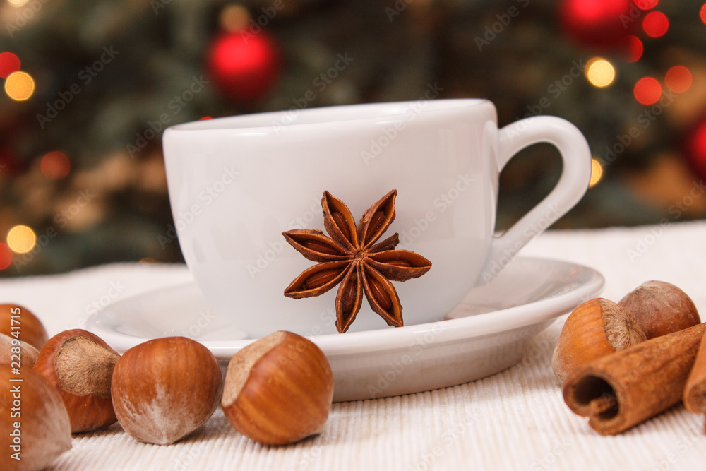 Hazelnuts, spices, cup of coffee or tea and christmas tree with lights in background Hazelnuts, spices, cup of coffee or tea and christmas tree with lights in background