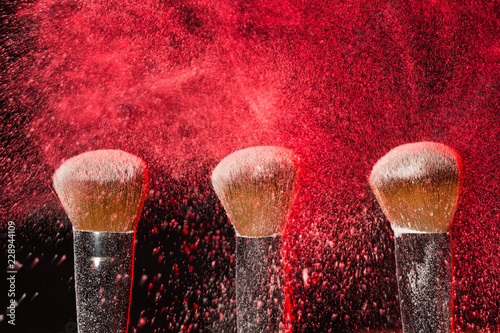 Make up, beauty, mineral cosmetic concept - powder brush on black background with red powder splashed on it