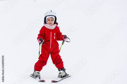 Little girl in red suit is skiing down a mountain