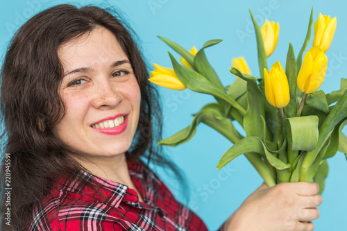 Close-up portrait of beautiful young woman with yellow tulips on blue background photo