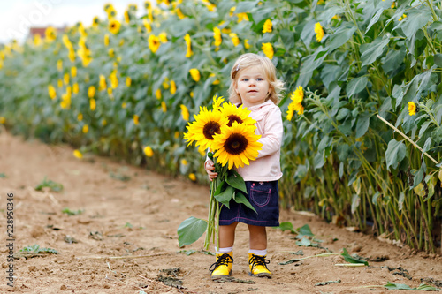Canvas Print Cute adorable toddler girl on sunflower field with yellow flowers