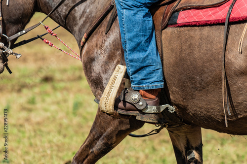 Lovely crafted belt and knife carrier and brown leather saddle, american cowboy warming up before rodeo performance on new ranch. Sunny event, United States national culture. © Edward R