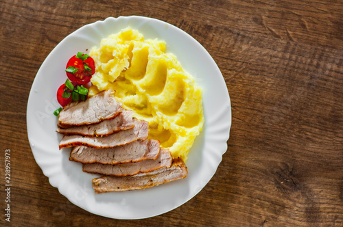 meat slices with mashed potatoes in white plate on wooden table background