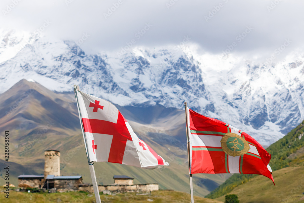 Flying flag of Georgia and flag of Georgian Border Police. With Svan's tower and mountains on the background, Svaneti.