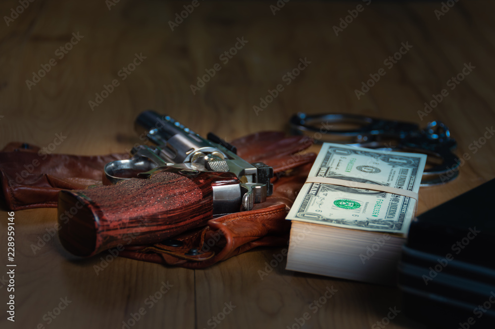 Obraz premium Dollar banknotes, shackles, document bag and carbiines put on gloves on a wooden table, to Dark business concept.
