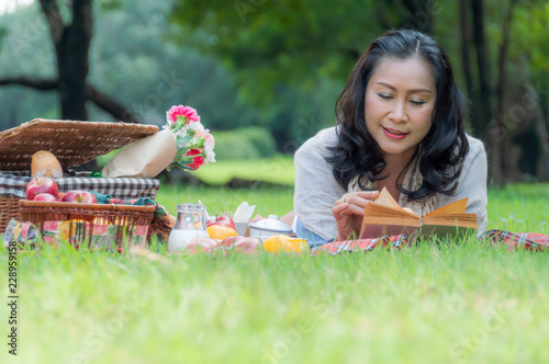 Asian women retirement are resting with a picnic in the garden with food and drink, breads, milk, and fresh fruits, apples and oranges And are enjoying their favorite books. to healt concept © Anatta_Tan