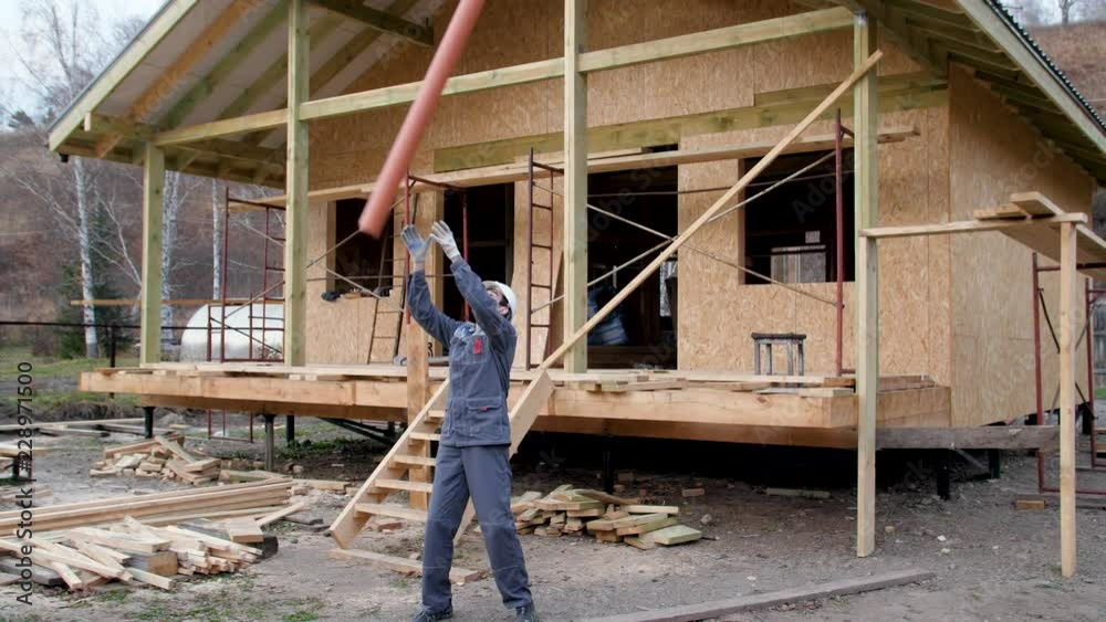 Construction worker on site juggle pipe. 4k slow motion 60 fps. Builder playfully carries a water pipe. Worker twists a water pipe against the background of a country house under construction.