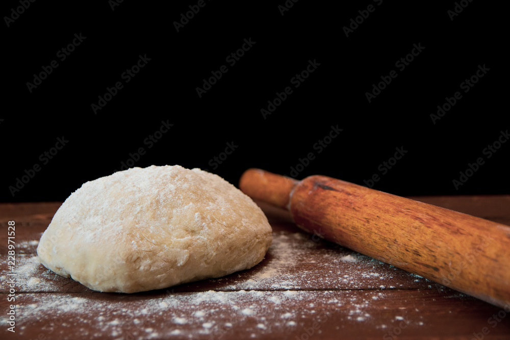 a lump of dough and a rolling pin lie on a wooden table on a black background a lump of dough and a rolling pin lie on a wooden table on a black background