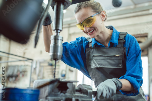 Woman worker in metal workshop using pedestal drill to work on piece