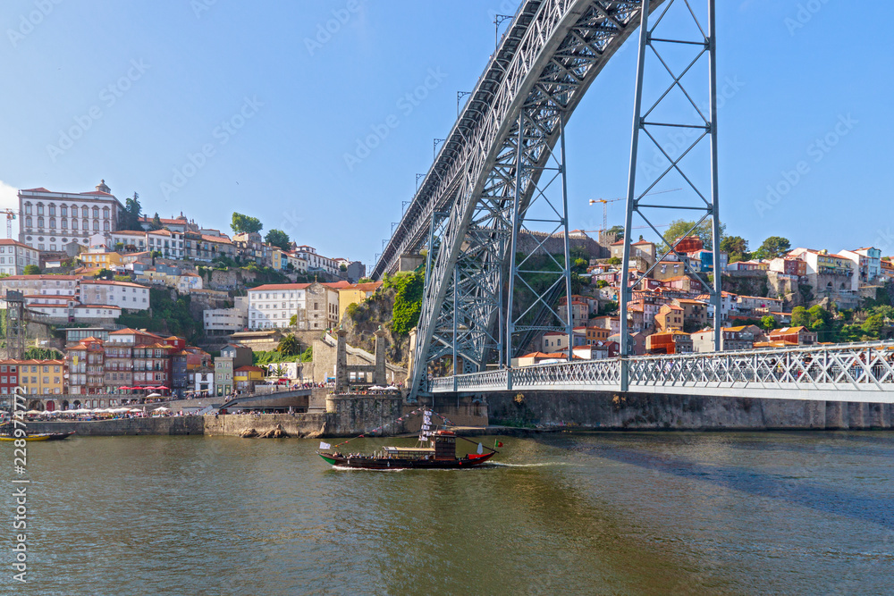The boat floats on the river Douro under the bridge Dom Luis I Bridge. Scenic view of Ribeira from Vila Nova de Gaia. Porto, Portugal
