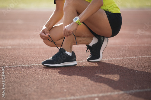 Young fitness woman runner tying shoelace on stadium