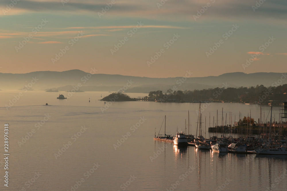 Sunset in Oslo, Norway. Panorama of the evening coast. Mountain landscape on the horizon. Lighthouse and sailing boats on a colorful sunset