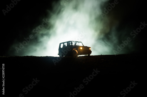 Off roader jeep silhouette on dark toned foggy sky background. Car with light at night. photo