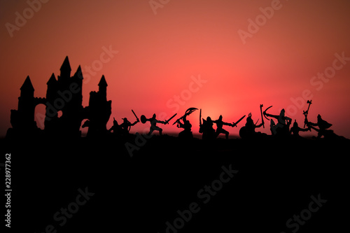 Medieval battle scene with cavalry and infantry. Silhouettes of figures as separate objects  fight between warriors on sunset foggy background.