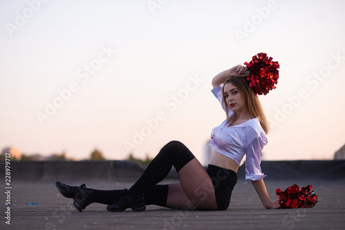 cheerleader with pompoms dancing outdoors on the roof at sunset photo