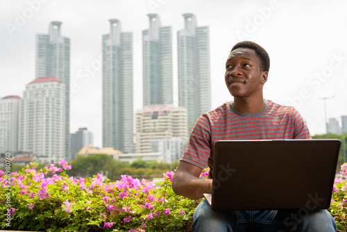 Young handsome African man using laptop computer in park