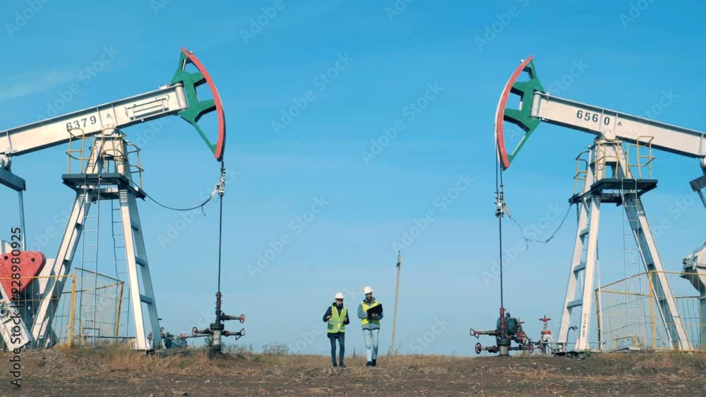 Engineers walk near working oil derricks, petroleum rigs. Oil industry concept. Engineers walk near working oil derricks, petroleum rigs. Oil industry concept.