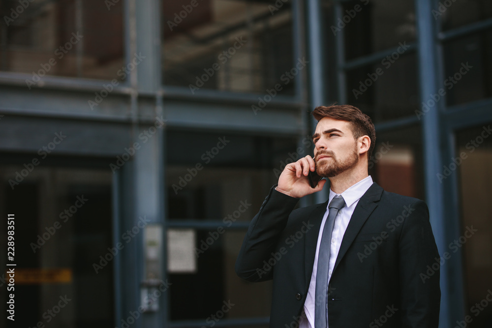 Businessman walking out of office and talking over mobile phone Businessman walking out of office and talking over mobile phone