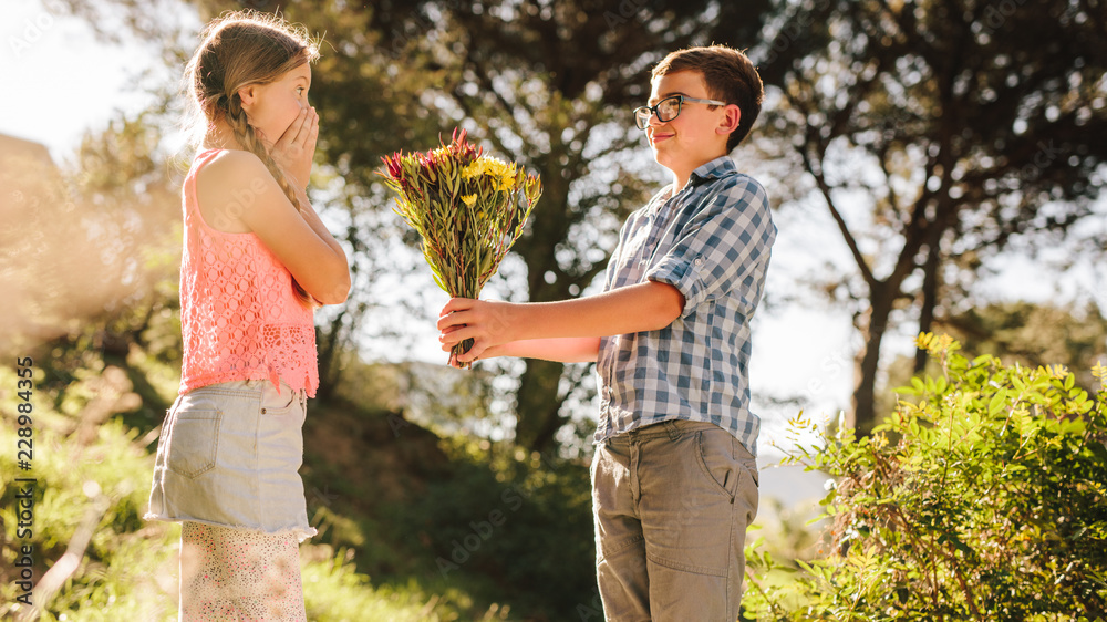Boy giving a bouquet of flowers to his girlfriend in a park Boy giving a bouquet of flowers to his girlfriend in a park