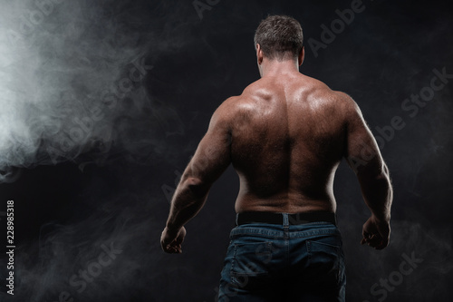 muscular man posing on black background showing his back