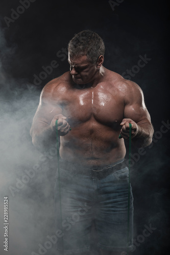 muscular man training with a harness on a black background in smoke
