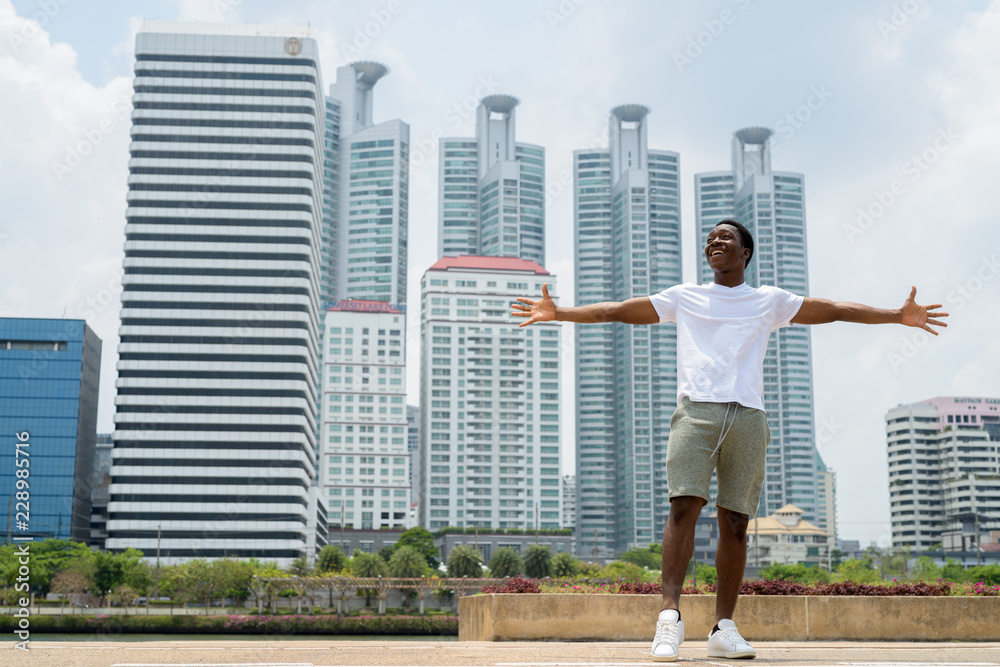 Young handsome African man with arms raised outdoors with cityscape background