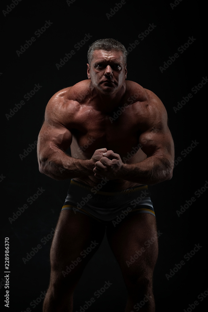 powerful muscular man shows biceps on a black background. Strength and fitness concept