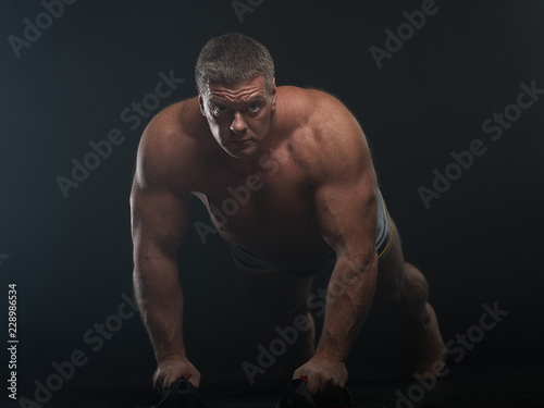 muscular man does pushups in the smoke on a black background © Vladimir