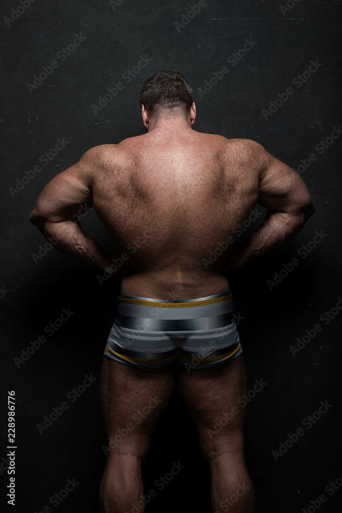 powerful muscular athlete shows off his back near a black grunge wall powerful muscular athlete shows off his back near a black grunge wall