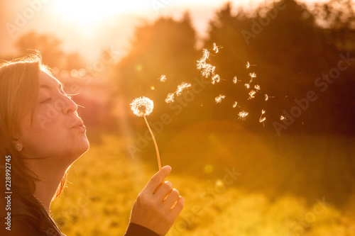 Junges Mädchen bläst Samen einer Pusteblume, Sonnenuntergang im Herbst mit Textfreiraum