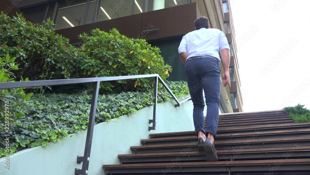 A businessman walks up a staircase by an office building - view from the ground A businessman walks up a staircase by an office building - view from the ground
