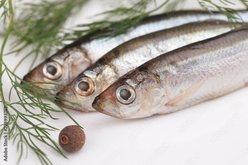 Salted sprats, dill and allspice berry on white plate