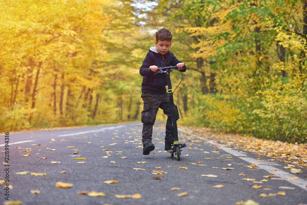 Cute boy riding scooter, outdoor in autumn environment on sunset warm light