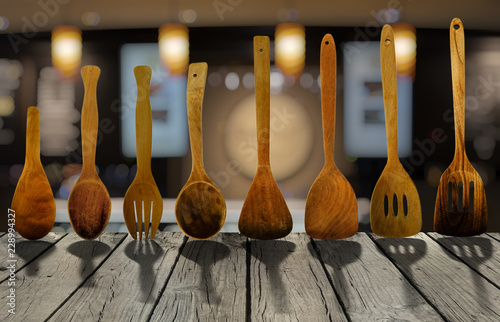 Wooden kitchen utensils on rustic wooden table with background of blur bokeh light in brown tone kitchen.