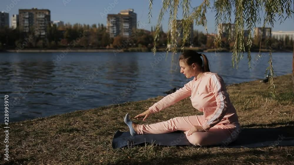Beautiful girl in a tracksuit on the city's waterfront does yoga. Beautiful girl in a tracksuit on the city's waterfront does yoga.